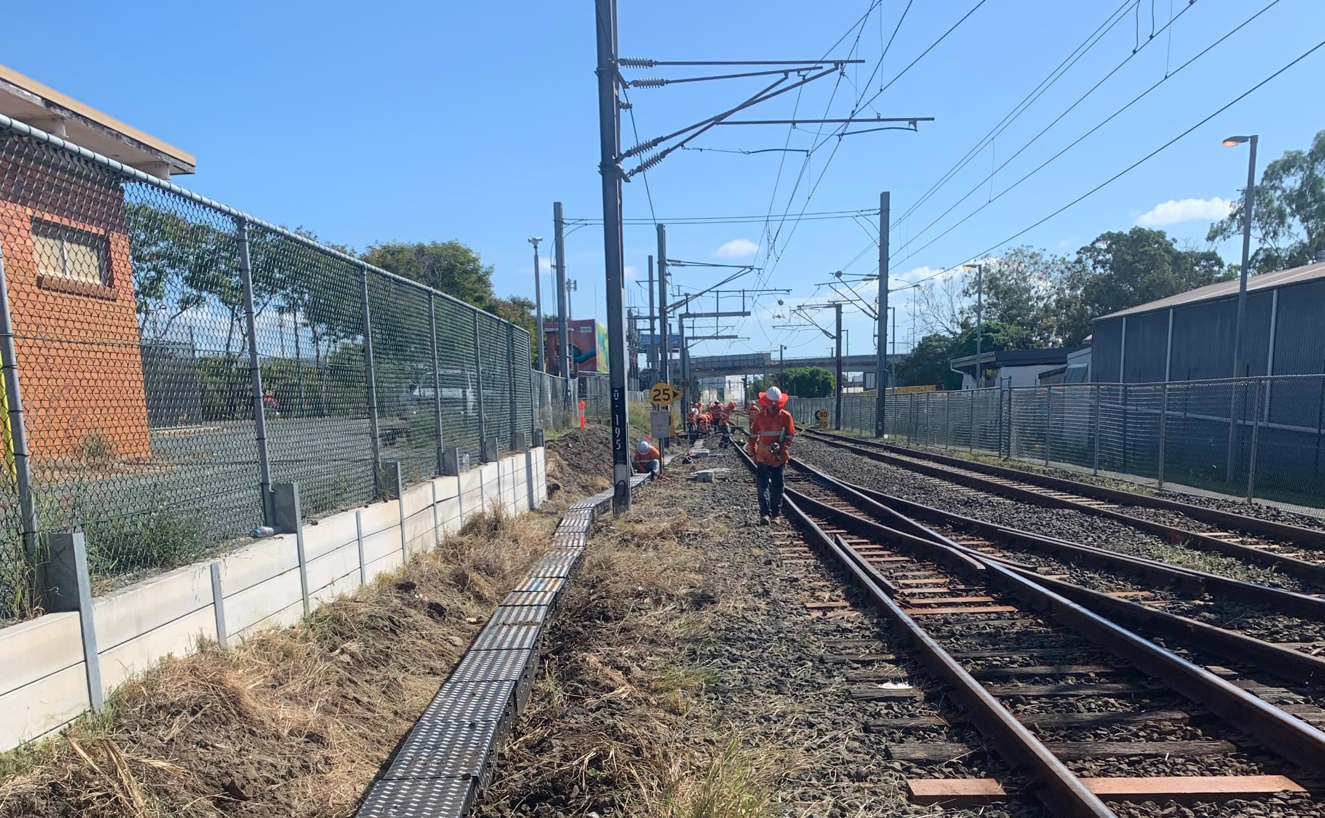 Crew laying pit and pipe alongside live rail tracks in a rail corridor