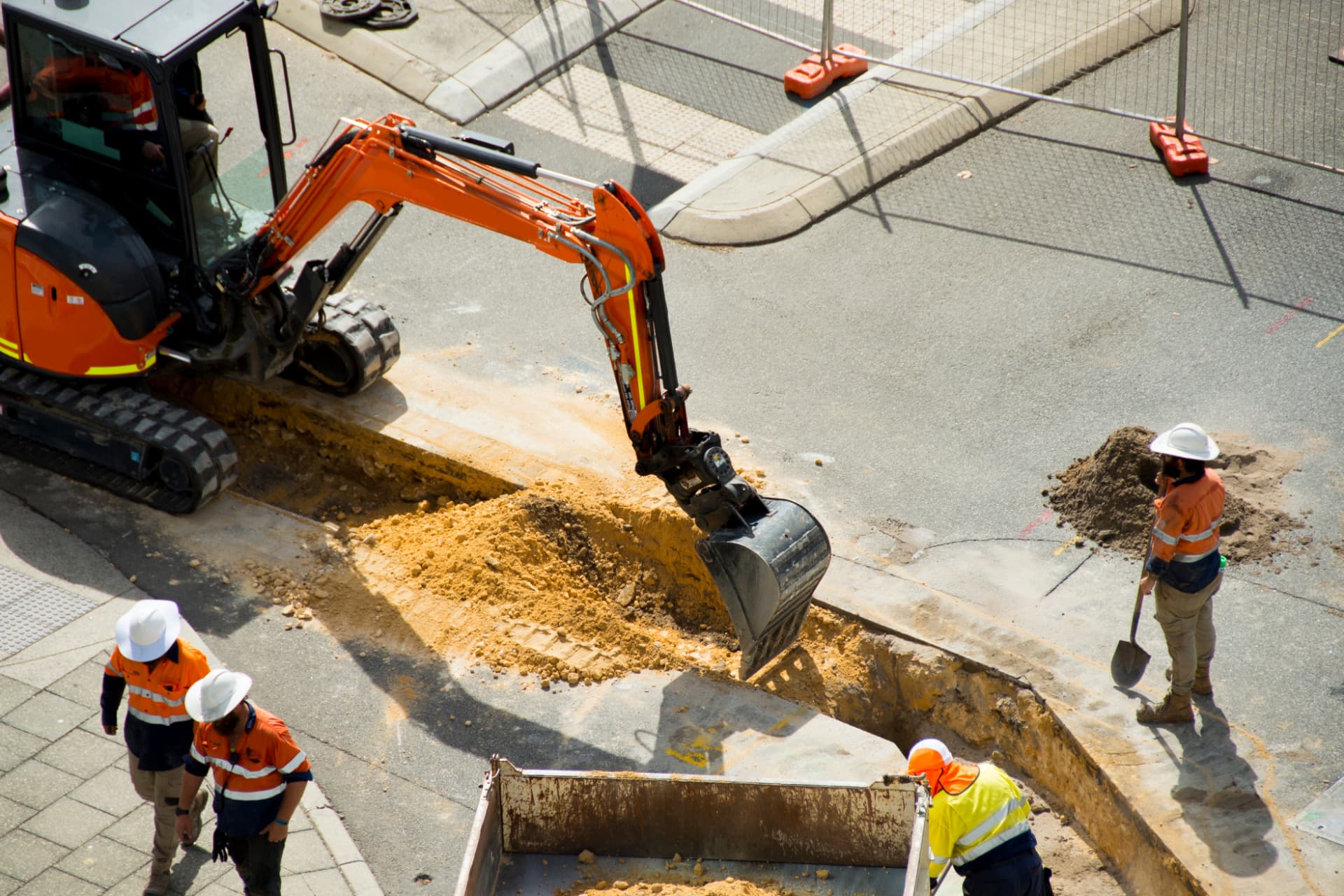 Excavator digging a trench for civil works while crew in hi-vis stand by